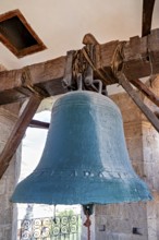 Large bell in an old tower made of wood and stone, with a bright sky in the background, The large