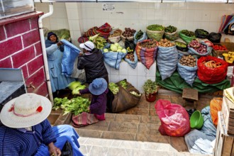 Women arranging vegetables in colourful sacks at a market stall in Bolivia, selling goods in the