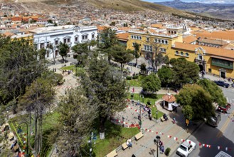 Square in a city with surrounding buildings and trees, lively with people, view over the city of