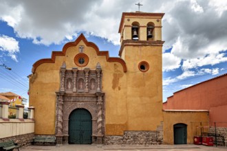 Colonial church with baroque bell tower and impressive wooden gate under a dramatic sky, The old