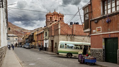 A lively street with colourful buildings against a backdrop of mountains and a bus. The atmosphere