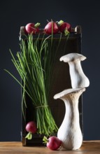 oyster mushrooms with radishes, chives and chillies on a wooden crate against a dark background