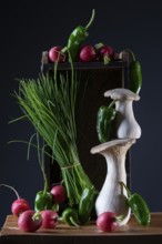 oyster mushrooms with radishes, chives and chillies on a wooden crate against a dark background