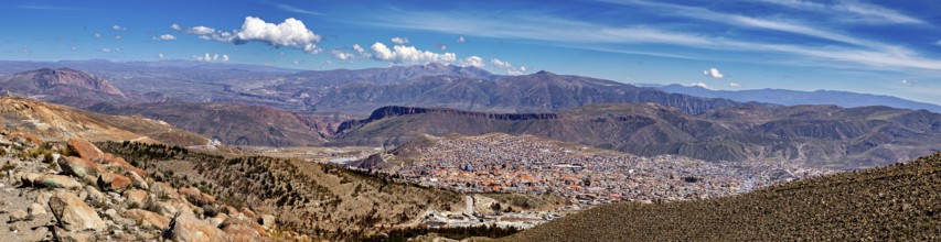 Panoramic view over a city in a wide valley with surrounding mountains under a cloudy sky, view