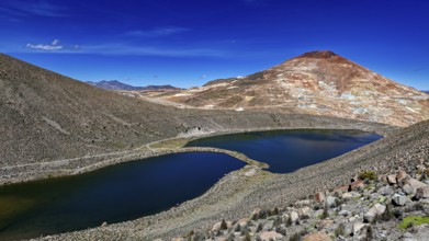 Volcanic mountain reflected in the lake, surrounded by barren landscape and under a bright blue