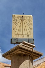 Stone sundial, mounted on a column, with dial and hands in front of a bright sky, The sundial of
