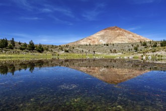 Volcanic mountain reflected in the calm waters of the lake under a clear blue sky, surrounded by