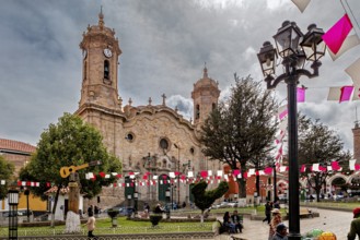 Lively square in front of a church with festive decorations and people, historic towers in the
