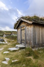 Wooden hut with grass roof and path in a rural setting under a blue sky with clouds, Peer Gynt