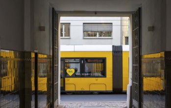 Urban environment in Berlin, a yellow tram can be seen through an open doorway. The scene captures