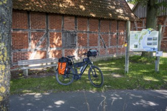 Bicycle in front of an old brick wall, next to it an information board in the sunshine, Weser cycle