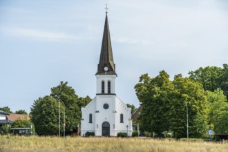 White church with tower and clock, embedded in a green landscape under a blue sky, Herford,