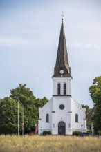 White church with high tower and clock, surrounded by trees under a clear sky, Herford, Westphalia,