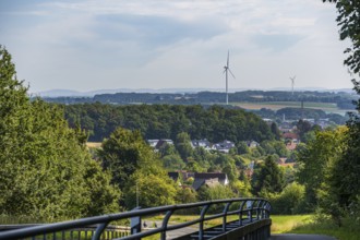 View of a village with wind turbines, surrounded by trees and fields, with a bridge in the