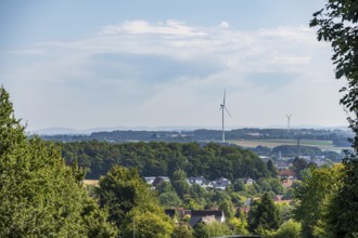 Landscape view with wind turbines and a village surrounded by green forests under a slightly cloudy