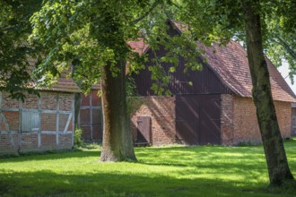 Large brick and wooden barn surrounded by trees and green grass, Weser cycle path, Schlüsselburg