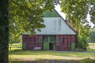 A traditional red and green half-timbered barn surrounded by trees on a sunny day, Gütersloh,
