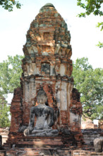 A Buddha statue seated before an ancient brick stupa, surrounded by greenery, exuding serenity in