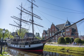 A historic sailing ship on a sunny day with a striking brick building in the background, The