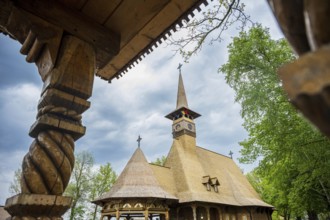 Detailed wooden church with decorative carvings and wooden roof, surrounded by trees, The Romanian