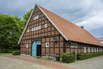 Traditional half-timbered house with red tiled roof and green surroundings under a cloudy sky,