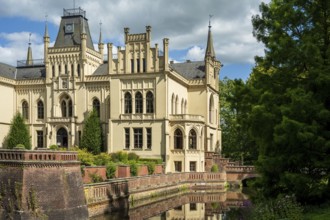 Gothic castle with moat and battlements, flanked by lush trees, Evenburg Castle, Leer, East Frisia