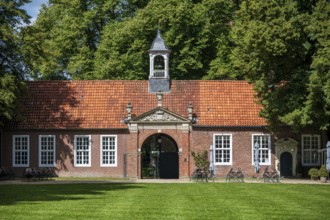 A historic building with a red tiled roof, a small bell tower, surrounded by green trees and a