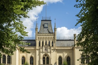 A Gothic castle with towers surrounded by green trees under a blue sky, Schloss Evenburg, Leer,