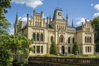 A magnificent Gothic-style castle surrounded by green trees and blossoming nature, Schloss