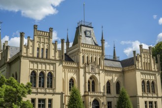 An imposing castle with Gothic elements and large windows under a blue sky, Schloss Evenburg, Leer,