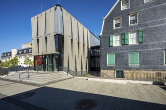 Modern glass façade next to an old house with coloured shutters, strong play of light and shadow,