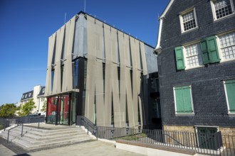 Modern building with a striking façade and large glass windows next to a traditional house under a