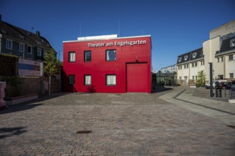 Theatre building in red with cobblestones surrounded by urban elements, high-contrast design,