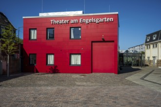 Red theatre building in front of a clear blue sky, modern style with paved forecourt, Theater am