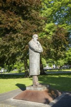 Side view of a stone statue of a pensive man in a green park with trees, statue of Friedrich Engels