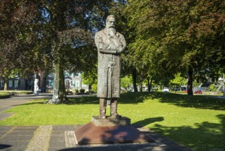 Statue of a man with crossed arms in a bright green park with trees in the background, statue of