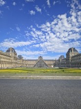 A grand panoramic view of the Louvre Palace with its iconic glass pyramid in the center under a