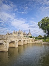 A picturesque stone bridge spans the still water leading to the magnificent Chateau de Chambord.