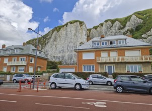 Row of houses with distinctive orange brickwork sits at the base of dramatic white chalk cliffs in