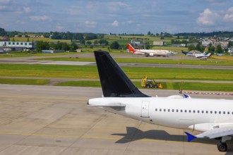 Passenger Airplane Taxiing on Runway and a Tractor Cutting the Grass in a Sunny Summer Day From the