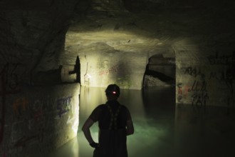 Person exploring illuminated, water-filled mine with graffiti, Ofenkaulen, Lost Place,