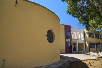 Gymnasium, Yellow modern building with round shapes, next to a tree under a blue sky, Historicism,