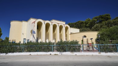 Primary school, Mediterranean building with arches and playground in front of vegetation,