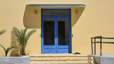 Gymnasium, A blue entrance to a yellow building with plants on the side, Historicism, Art Deco,
