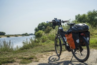 A bike with panniers stands on a sunny riverbank, embedded in nature, Weser cycle path, Weser,