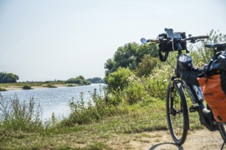 A bicycle stands on the riverbank, surrounded by a green landscape under a clear sky, Weser cycle