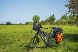 A bicycle stands on a green meadow under a blue sky, accompanied by light shadows of nature, Weser