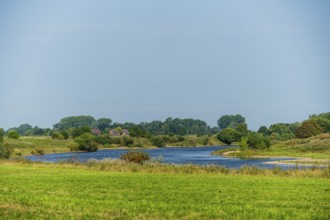 River flows through a green landscape under a blue sky, surrounded by trees and meadows, Weser