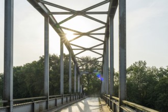 Metal bridge with sunlight, surrounded by trees, shows modern style, Weser cycle path, district of