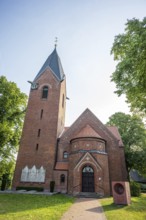 Brick church with Gothic tower and clock, surrounded by green trees under a blue sky, Weser cycle